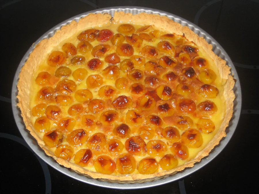 Tarte aux mirabelles dorée dans son moule cannelé, fruits glacés et appareil pris